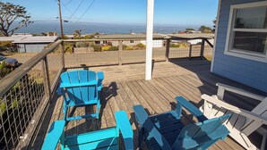 Une terrasse en bois avec des chaises Adirondack bleues, une rambarde et une vue sur l’océan.