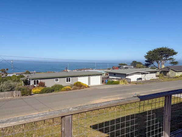 A coastal residential area with houses, a clear sky, and the ocean in the background.