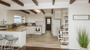 Une cuisine spacieuse avec des meubles blancs, un îlot central doté de tabourets et un plafond en bois.