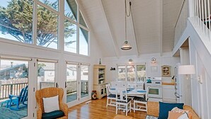 Amplia sala de estar con ventanas grandes, una mesa de comedor y una zona de cocina.