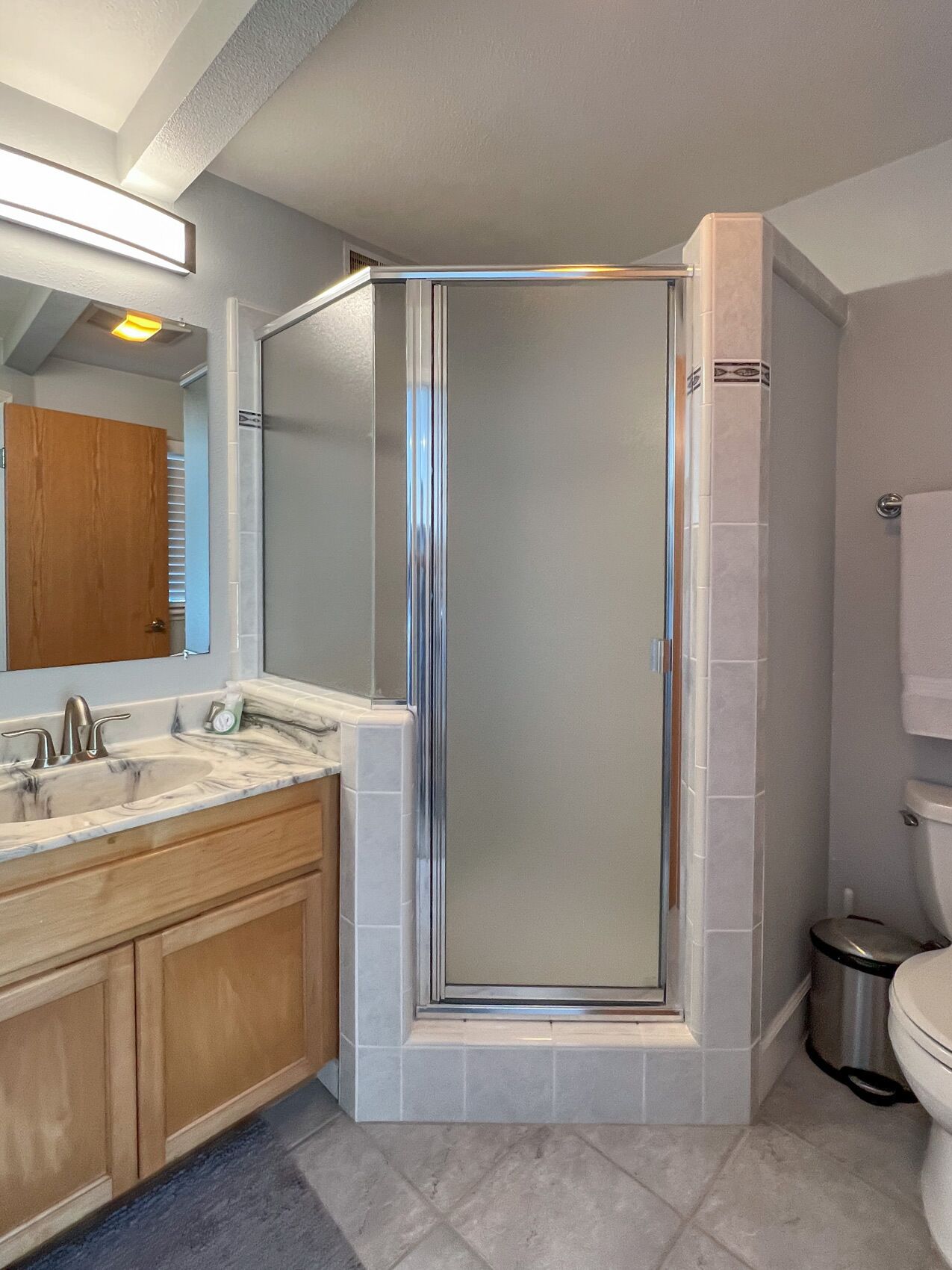 A modern bathroom with a glass-enclosed shower, a marble sink, wooden cabinets, and a toilet.