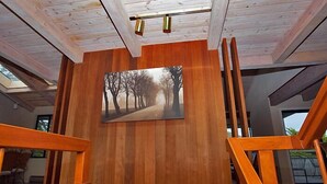 A modern interior with wooden paneling, a staircase, and a painting of a tree-lined path.