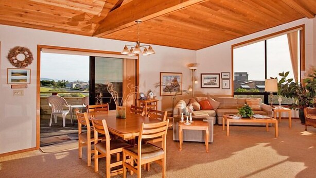 A spacious living area with a wooden ceiling, a dining table with chairs, a sofa, and a coffee table. There is a large window providing a view of the outdoors. - Boccabella - Quite south side location, expansive views. (Bodega Bay)
