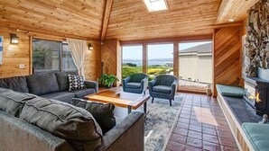 A cozy wooden interior with a sofa, chairs, a fireplace, and large windows offering a view. - Condors Nest - 10th green w/ocean views , . (Bodega Bay)
