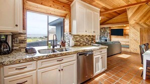 A kitchen with wooden ceiling beams, a stone backsplash, and a large window. - Condors Nest - 10th green w/ocean views , . (Bodega Bay)