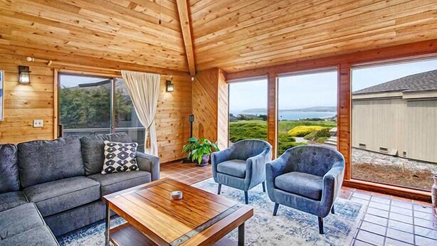 A cozy room with a wooden ceiling, a sofa, two armchairs, a coffee table, and large windows offering a view of the landscape. - Condors Nest - 10th green w/ocean views , . (Bodega Bay)