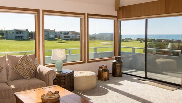 Amplia habitación con ventanas grandes que ofrecen vistas a un campo de golf y al océano.