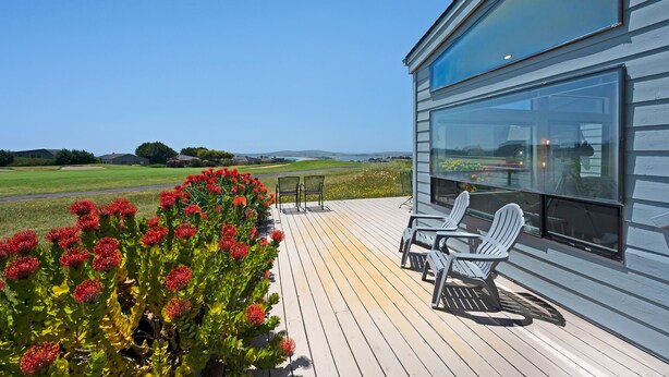 A modern house with a large glass window, a wooden deck, and outdoor seating. - Dabbling Duck - Light, open, warm home on the 14th fairway, great views (Bodega Bay)