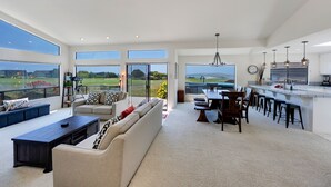 A spacious living room with a large sofa, coffee table, and a dining area with a kitchen counter and bar stools. - Dabbling Duck - Light, open, warm home on the 14th fairway, great views (Bodega Bay)