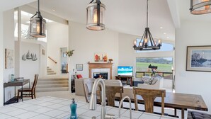 A spacious living area with a fireplace, a dining table, and a kitchen with a sink. - Dabbling Duck - Light, open, warm home on the 14th fairway, great views (Bodega Bay)