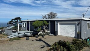 Eine Garage mit einer weißen Tür, ein überdachter Balkon mit Gartenmöbeln und Blick auf den Ozean.
