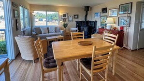 Ein gemütliches Wohnzimmer mit Sofa, Esstisch, Stühlen, Kamin und gerahmten Bildern an der Wand.