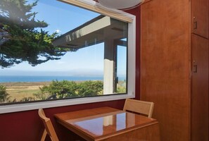 Una habitación con una mesa de madera y una ventana que da a un paisaje con árboles y vistas al océano.