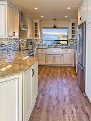A kitchen with light-colored cabinets, a granite countertop, a stainless steel refrigerator, and a window with a view of greenery outside. - Paradise on the Bay - Nice ocean views, 1 level (Bodega Bay)