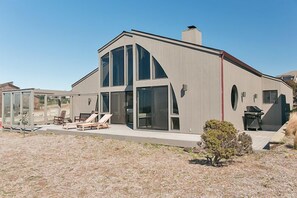 A modern house with large windows, a patio with lounge chairs, and a small garden.