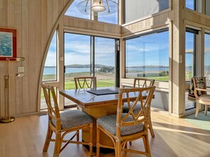 A dining area with a wooden table and chairs, large windows offering a view of the landscape, and a pendant light above the table.
