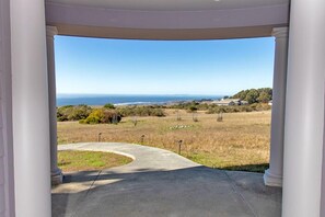 A view from a covered porch with a concrete pathway leading to a grassy area and a distant view of the ocean.