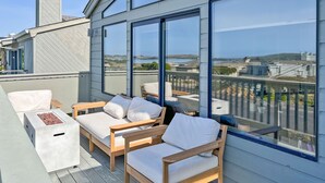 A rooftop terrace with a view of the ocean, furnished with wooden chairs and a small table.