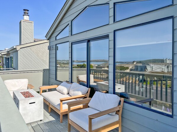 A rooftop terrace with a view of the ocean, furnished with wooden chairs and a small table.