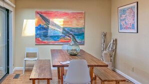 A dining area with a wooden table, white chairs, and a large abstract painting on the wall.