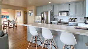 A modern kitchen with a central island, bar stools, and a dining area with a view.