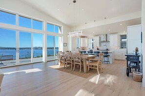 A spacious kitchen with large windows, a dining area with wooden furniture, and a view of the water.
