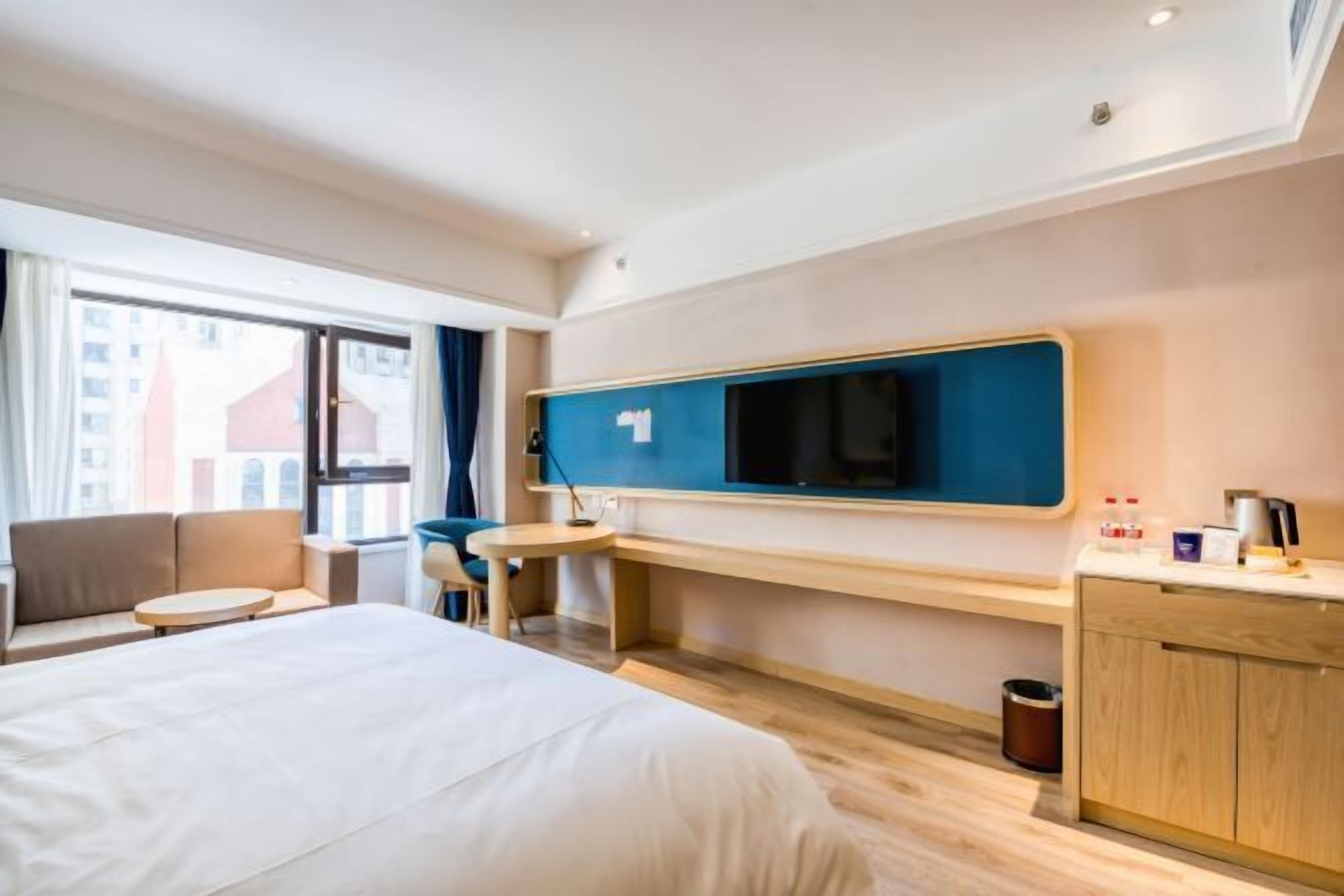 Una habitación de hotel moderna con una cama grande, un escritorio, un televisor y vistas a la ciudad por la ventana.