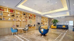 Un hall d’entrée agrémenté d’un globe servant de pièce maîtresse, d’étagères en bois où sont exposés divers objets, d’un coin salon avec des fauteuils bleus et d’un lustre.