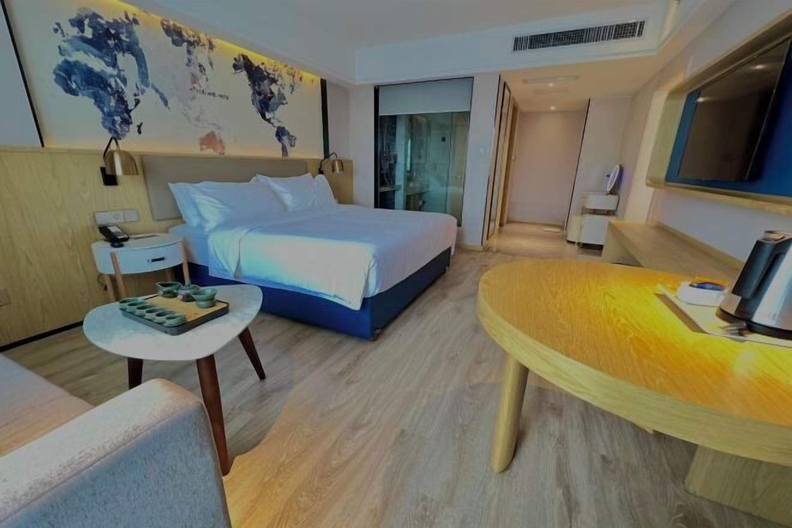 A modern hotel room with a large bed, a small desk, a round wooden table, and a world map on the wall.