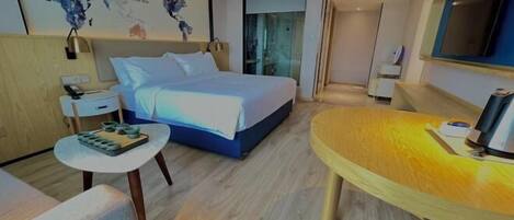 A modern hotel room with a large bed, a small desk, a round wooden table, and a world map on the wall.