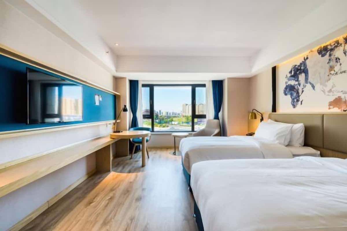 A hotel room with a bed, a desk, a chair, a TV, and a window with a city view.