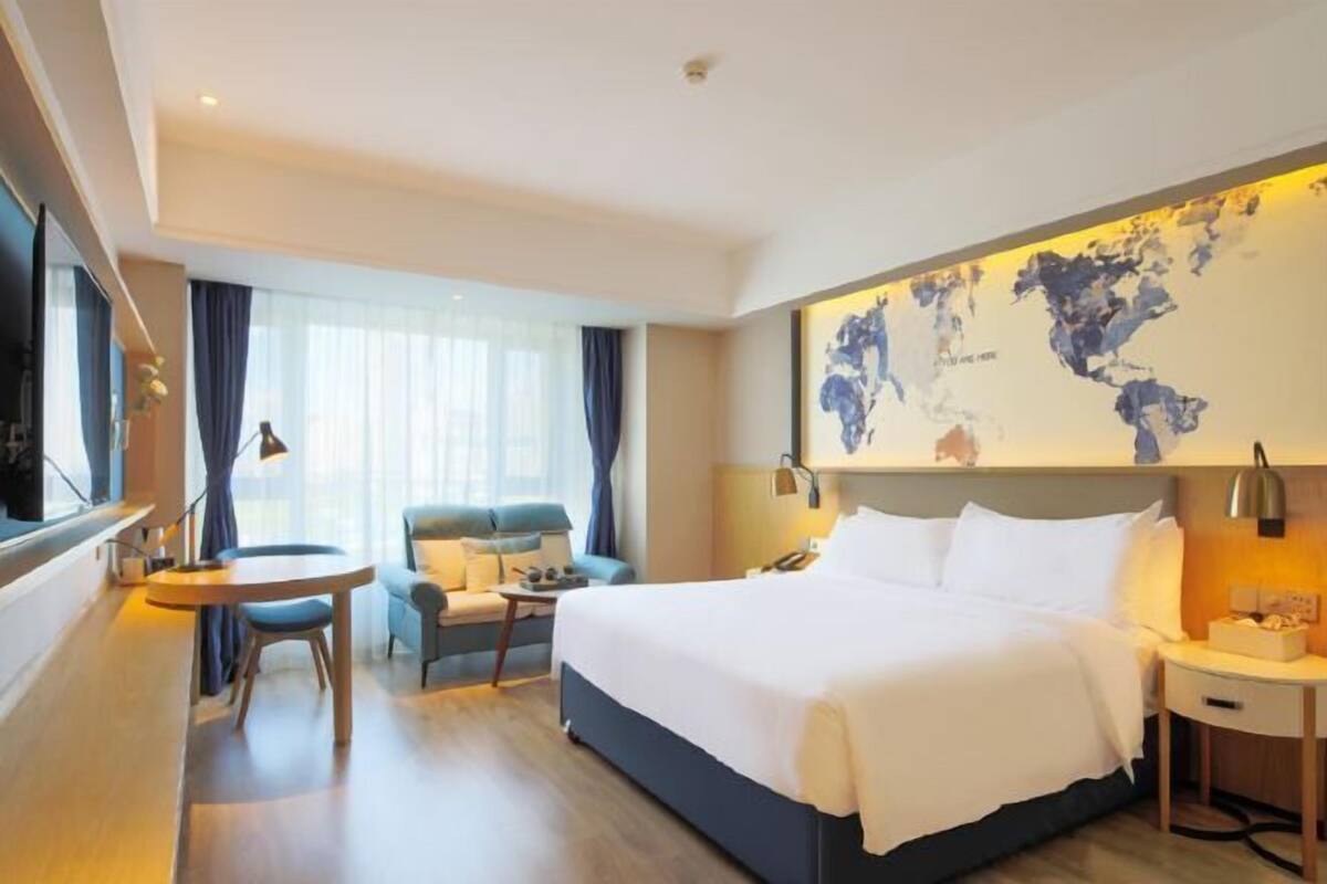 A hotel room with a large bed, a desk, a chair, a map on the wall, and a window with curtains.