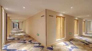 Un couloir d’hôtel avec un sol à motifs, des portes portant l’indication du numéro de chambre et des panneaux indiquant les sorties de secours.