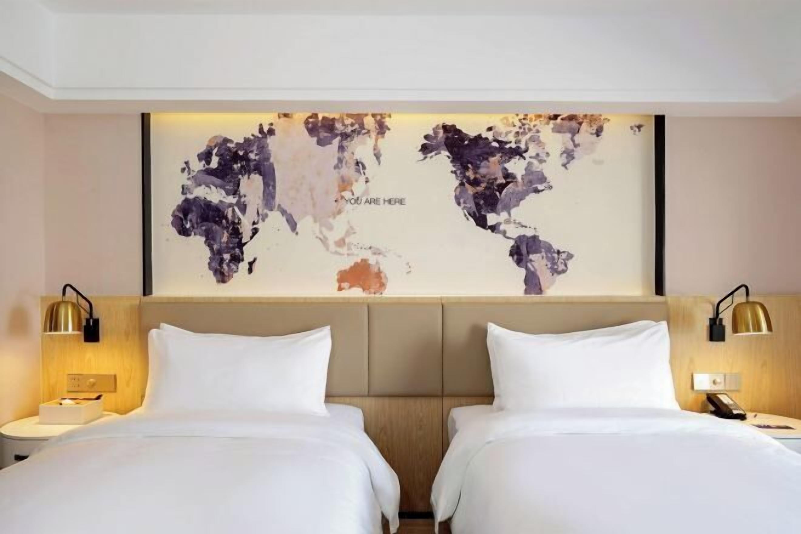 A hotel room with two beds, a world map artwork on the wall, and bedside lamps.