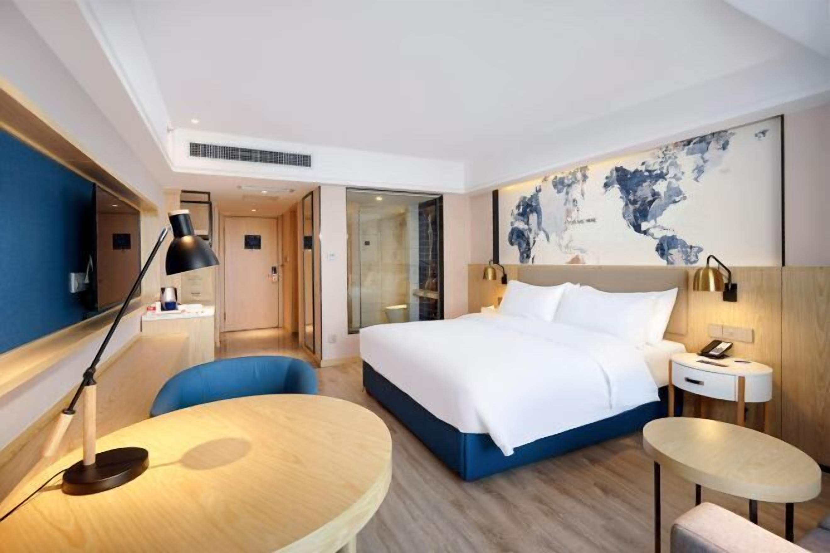 A modern hotel room with a large bed, a desk, a chair, and a round table.