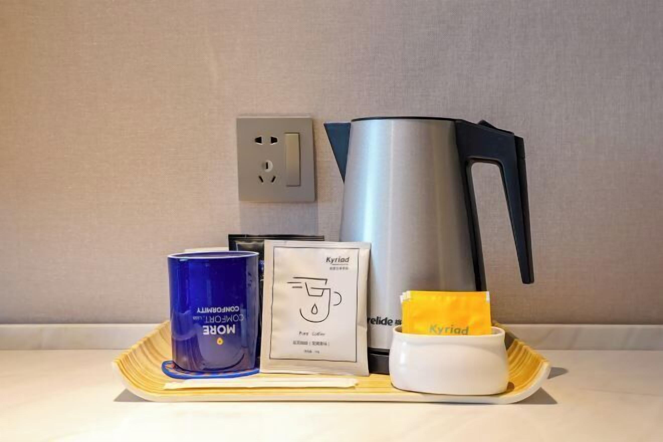 Una bandeja con una vela azul, una cápsula de café, una cafetera y un paquete amarillo sobre una mesa.