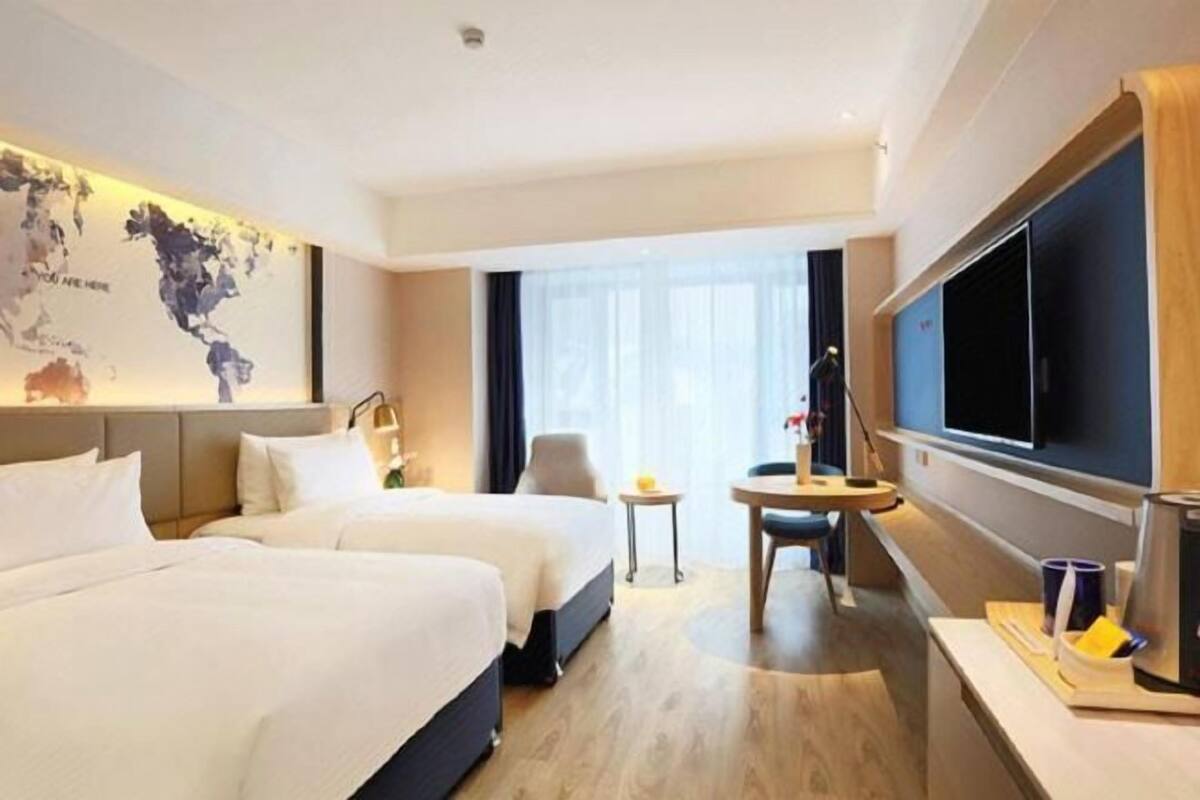 A hotel room with two beds, a TV, a small table, and a window with curtains.