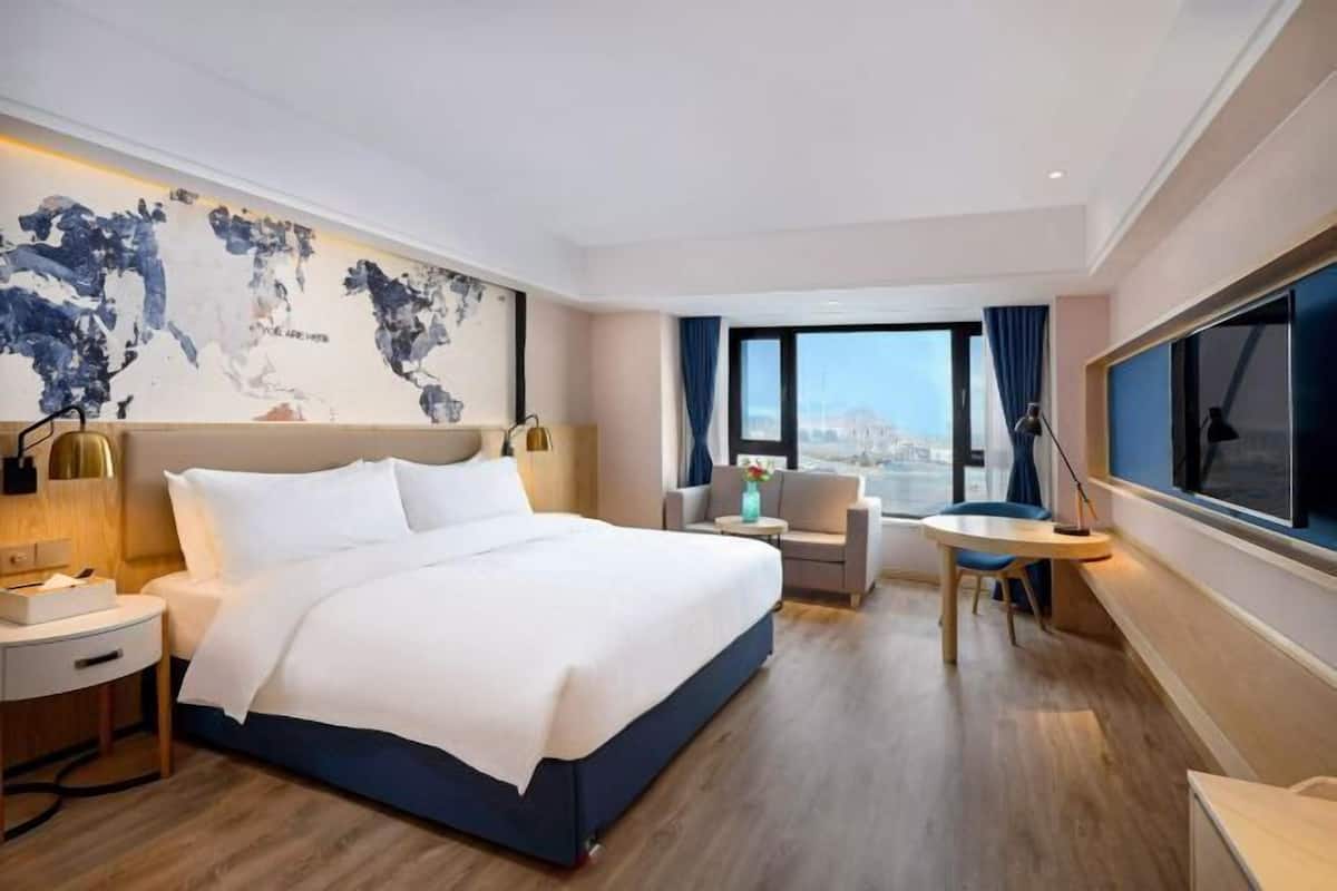 A hotel room with a large bed, a desk, a chair, and a view of the city.