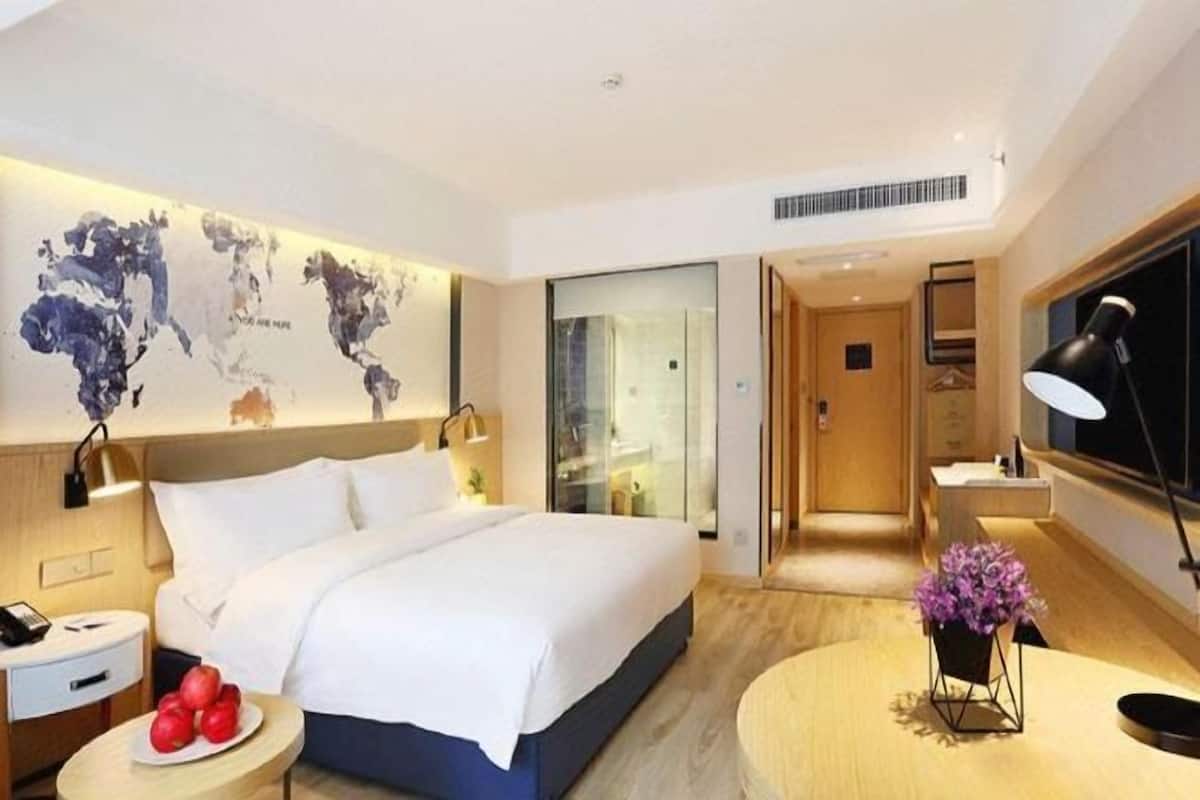 A modern hotel room with a large bed, a desk, a world map on the wall, and a view into the bathroom.