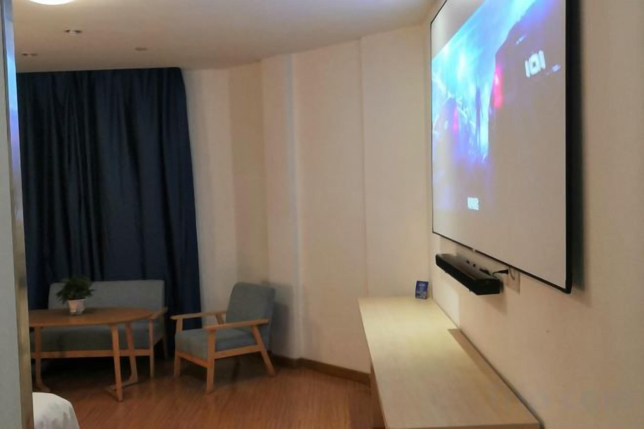 A room with a projector screen, a table with chairs, and a blue curtain.