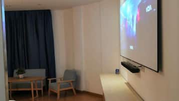 A room with a projector screen, a table with chairs, and a blue curtain.