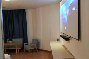 Una habitación con pantalla de proyector, una mesa con sillas y una cortina azul.