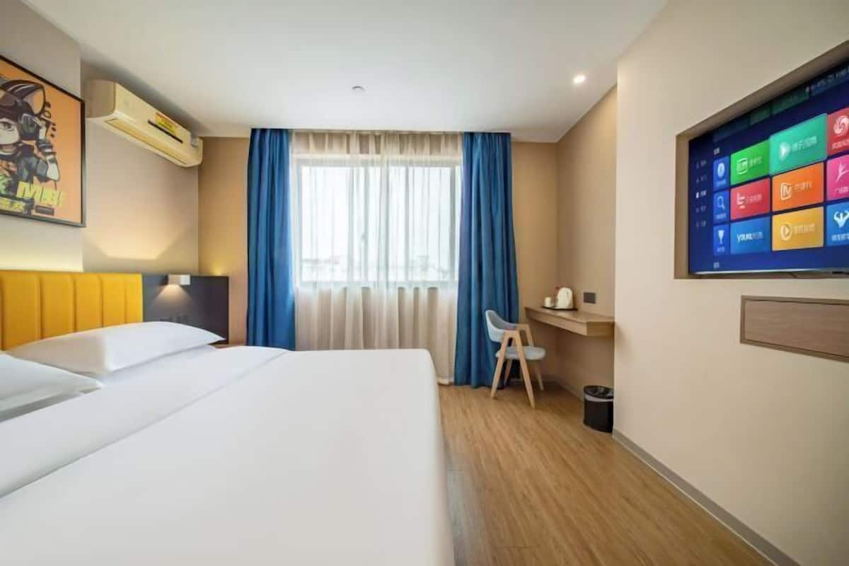 Habitació d'hotel amb llit, escriptori, cadira, televisió i finestra amb cortines.