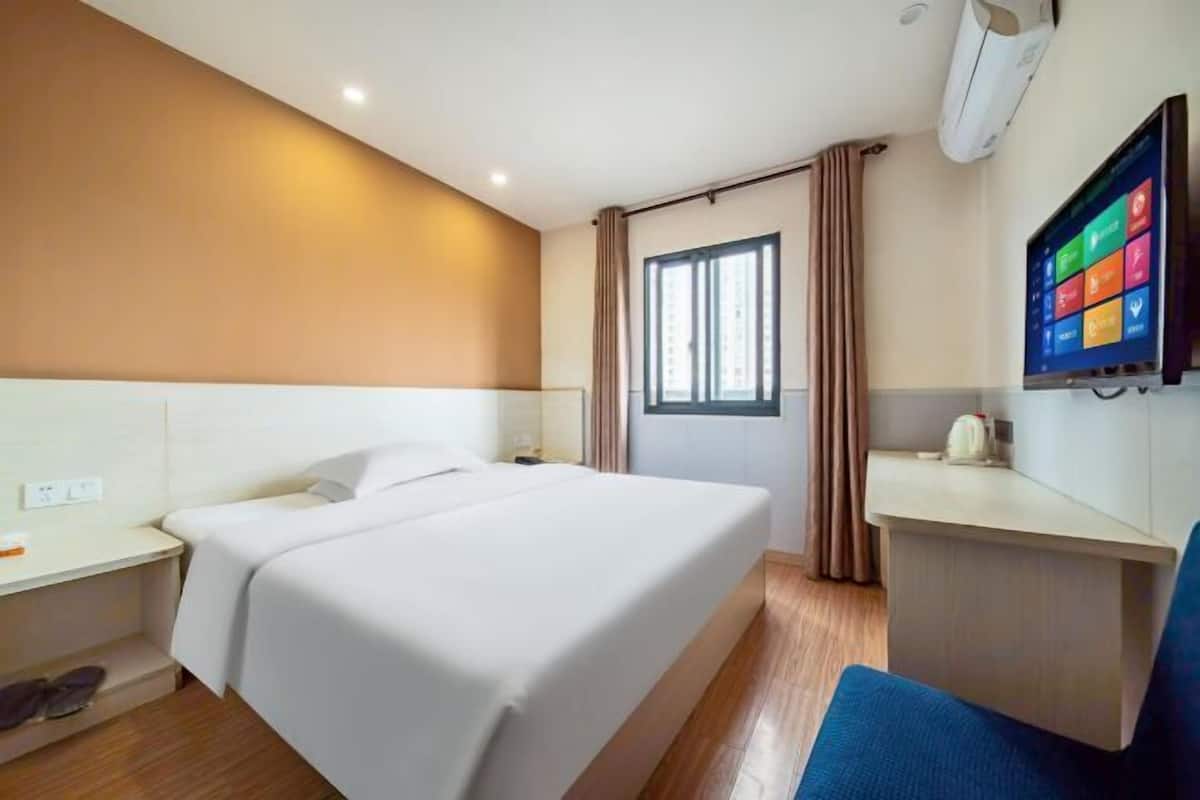 Habitació d'hotel amb llit, taula de nit, televisió i finestra amb cortines.