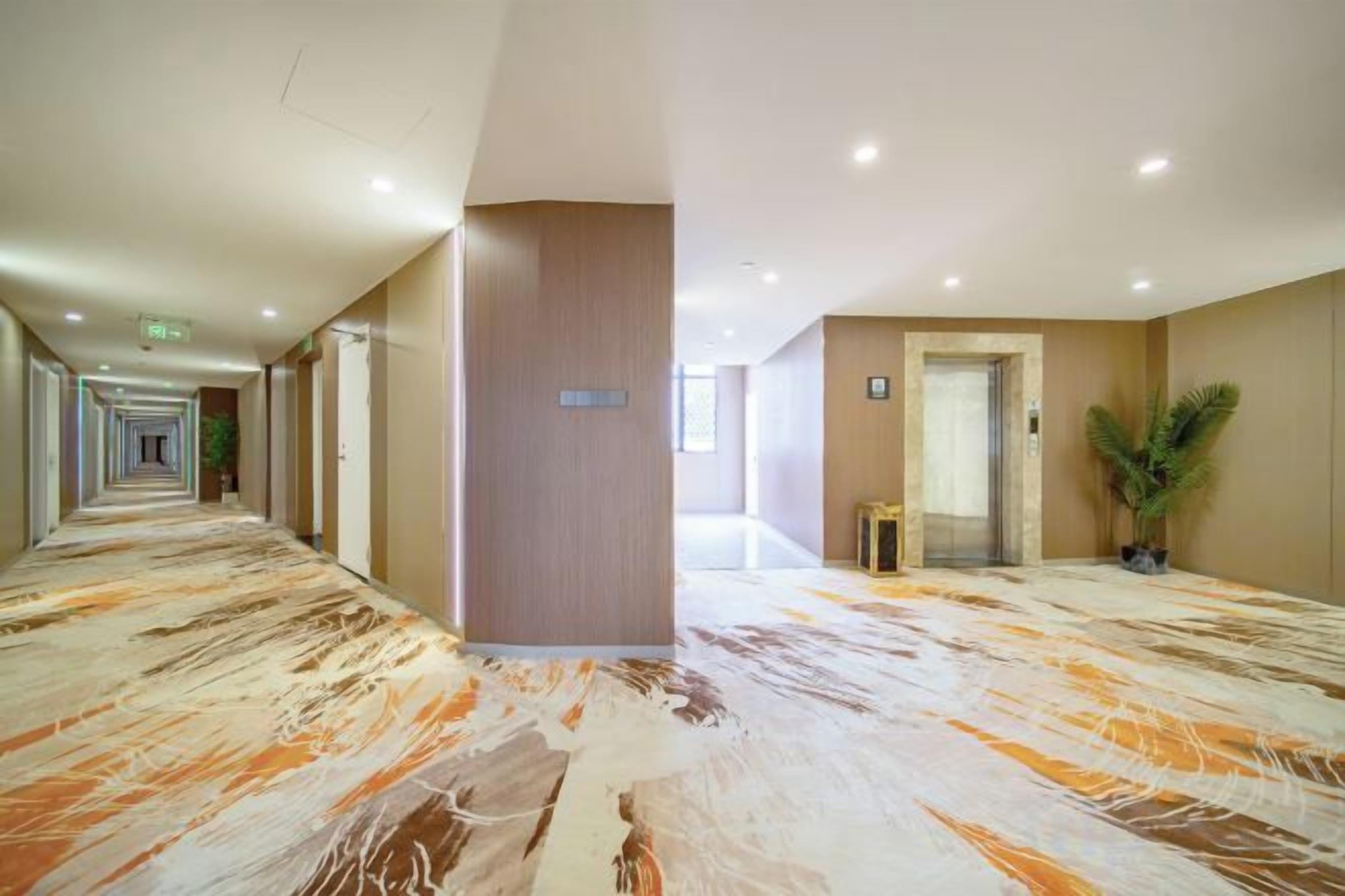 A hotel corridor with a marble floor, doors on both sides, and a potted plant.