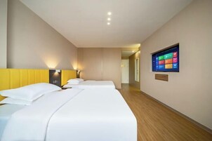 A hotel room with two beds, a flat-screen TV mounted on the wall, and a wooden floor.
