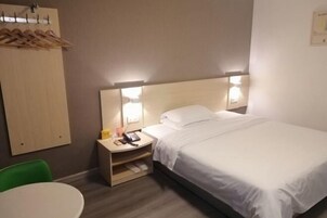 Una habitación de hotel con cama, mesita de noche, lámpara, silla y perchero.