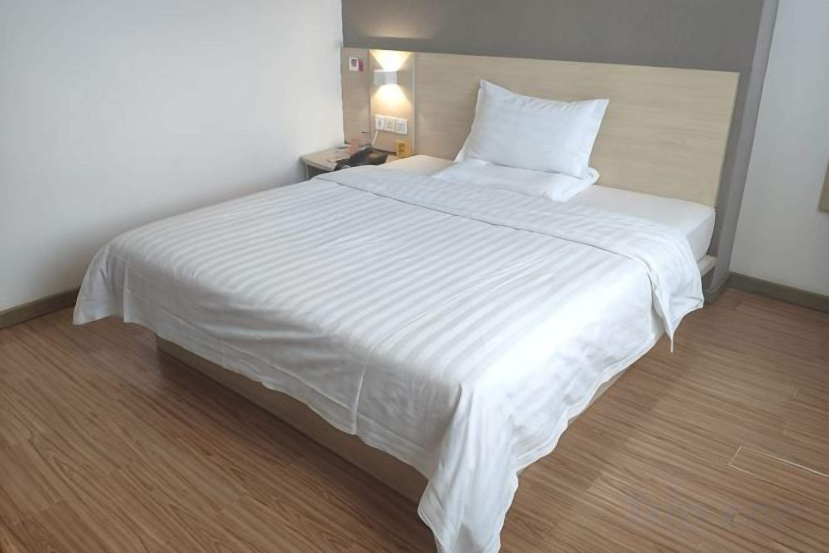 A neatly made bed with a wooden headboard, a bedside table with a lamp, and a wall-mounted light fixture.