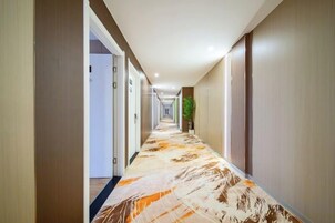Pasillo de hotel con puertas a ambos lados, alfombra estampada y una planta en el centro.