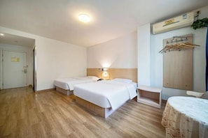 A hotel room with two beds, a bedside table, a lamp, a wardrobe, and a wooden floor.